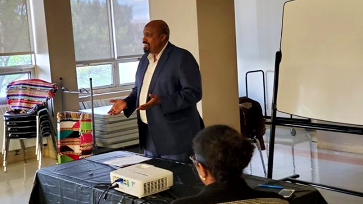 Karod standing behind a desk, speaking inside the Somali Centre, in Ottawa