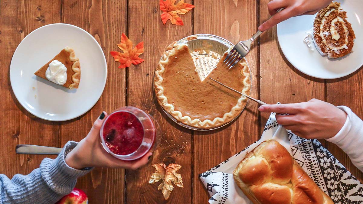 A picture of table with pumpkin pie, bread, a glass of sangria, an apple, and other desserts on it.