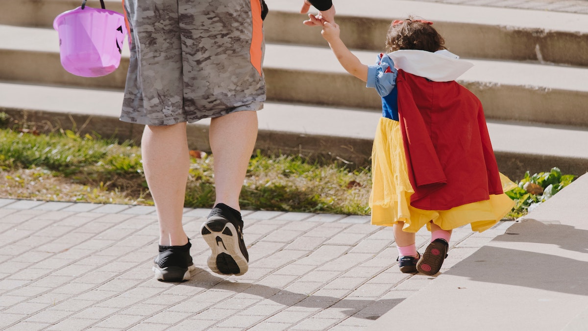 A child holds their parents' hand on their way to go trick or treating