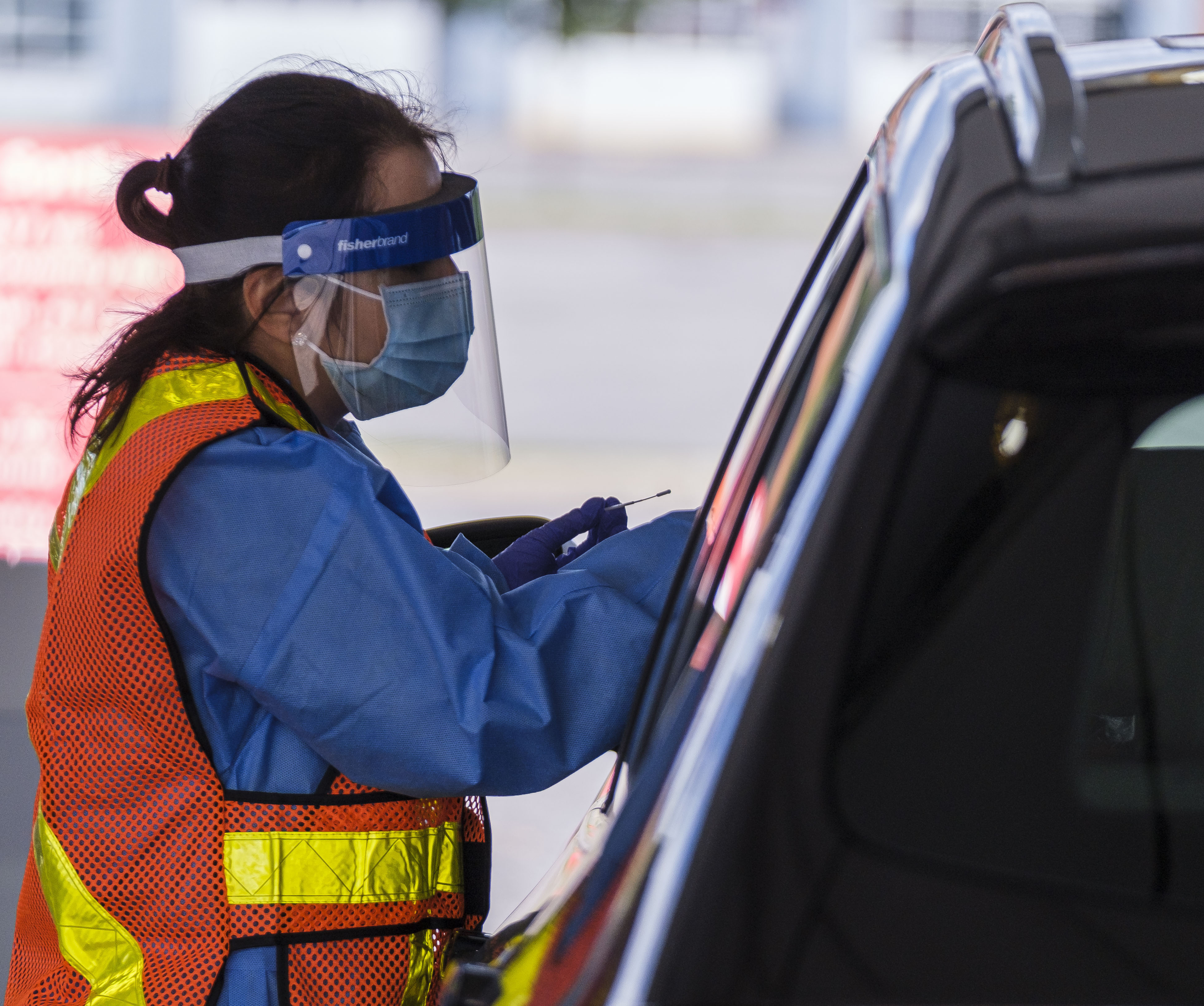 A COVID tester holds a swab after testing someone in their car.