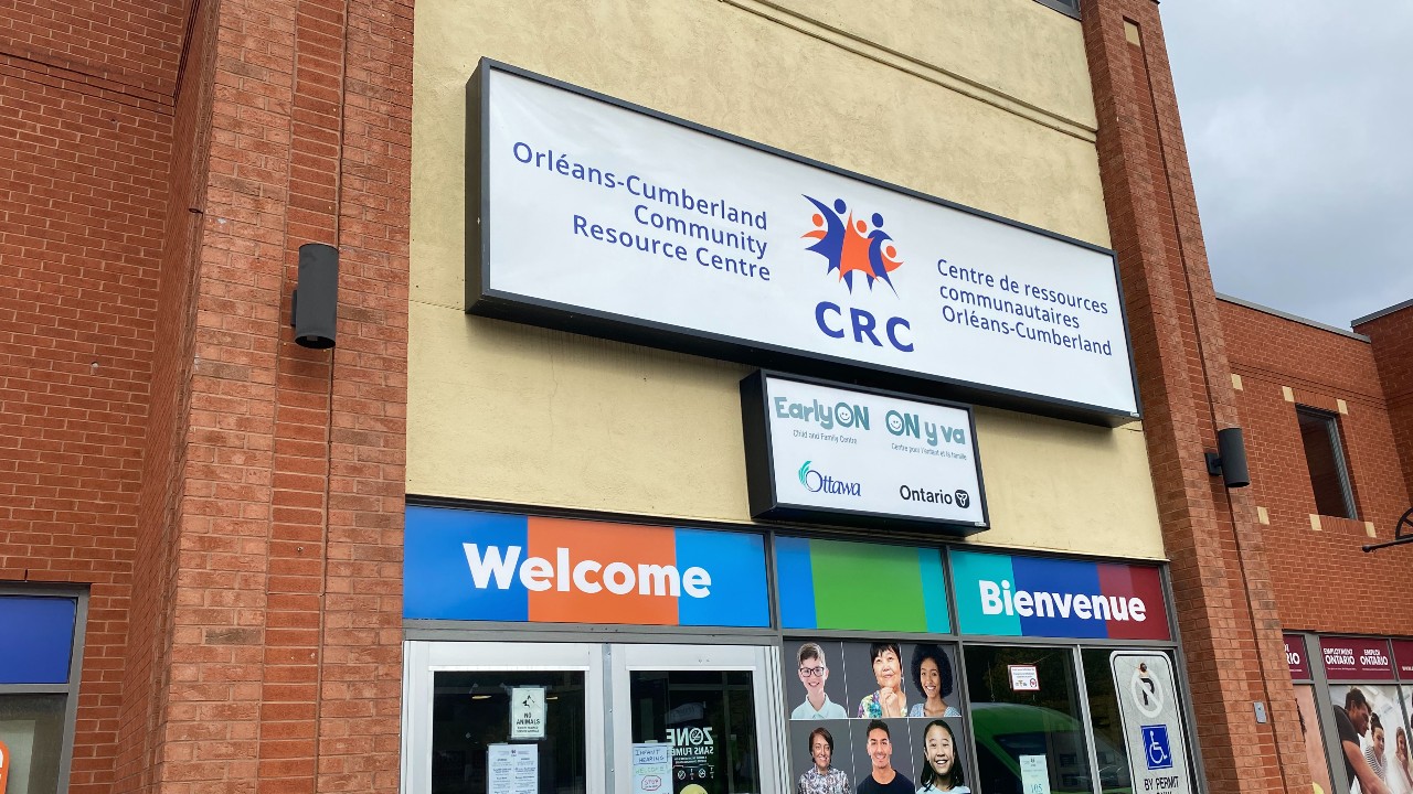 Front entrance of the Orléans-Cumberland Community resource centre, with a sign above the door saying "Orléans-Cumberland Community Resource Centre/Centre de resources communautaires Orléans-Cumberland," and a bilingual welcome sign below.