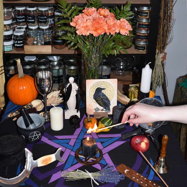 eclectic photo of an altar containing: a black light candle, lavender, an apple, picture of crow, among other things.