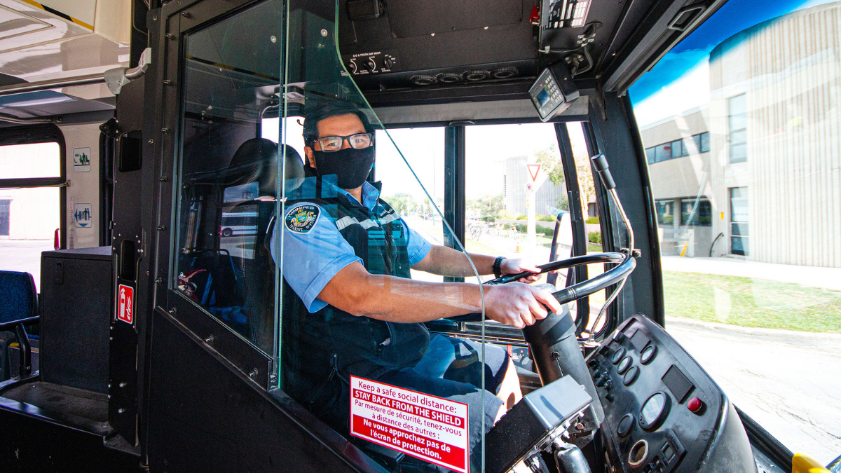 A bus driver sits behind a plexiglass shield wearing a facemask.
