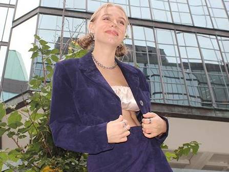 Woman wearing a blue jacket and skirt in front of buildings.