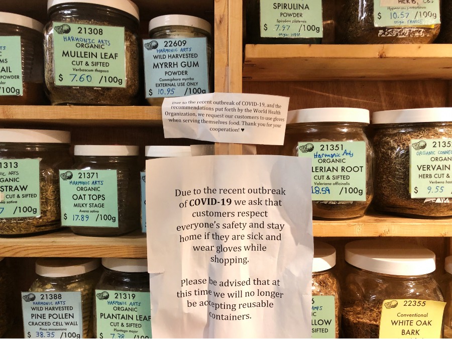 Low waste grocery store 'Herb and Spice Shop' sign posted on their self serving spice shelf describing why they no longer allow customers to bring in their own containers due to pandemic.