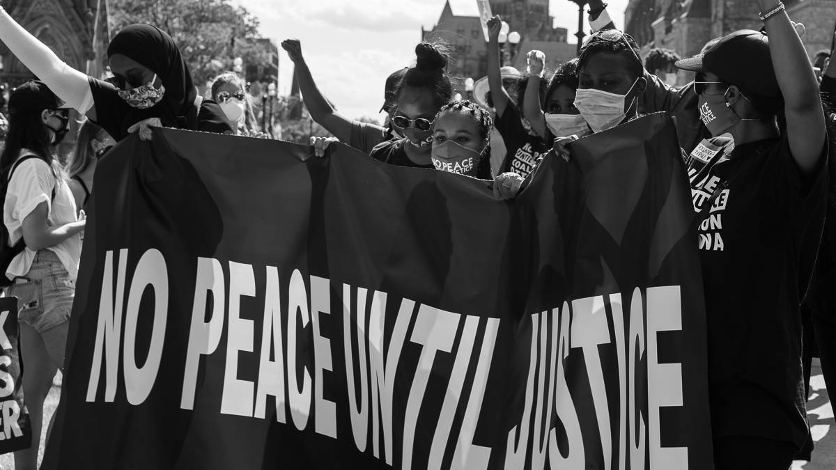 Photo of protestors at the Black Lives Matter protest in Ottawa holding a sign that says No Peace Until Justice.