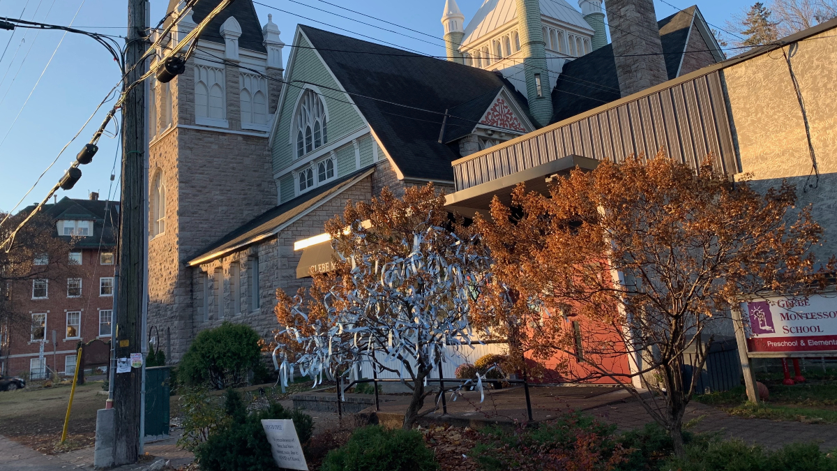 A tree with blue ribbons tied to it is seen in front of a church.