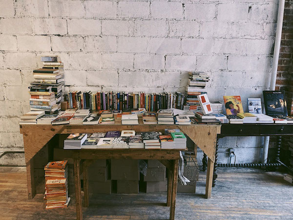 Three desks covered in books against a white brick wall.