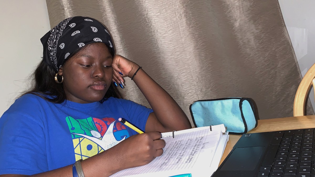 A girl studies at her desk, with school papers and a lapop in front of her.