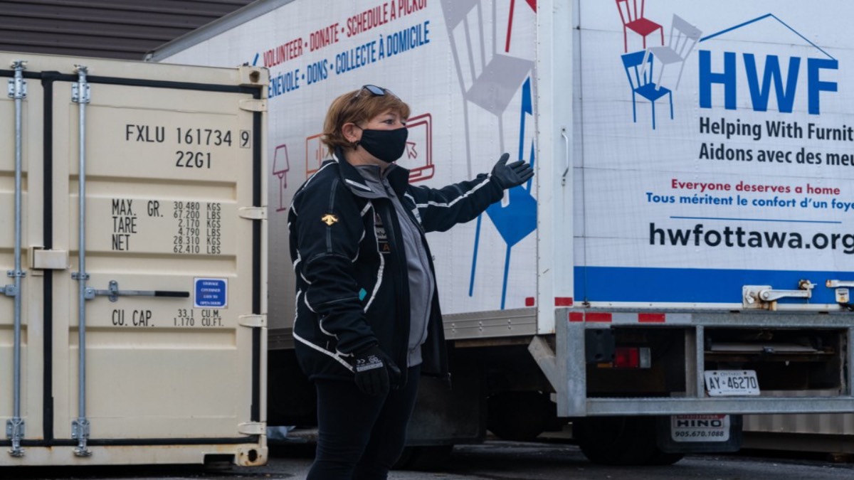 Nathalie Maione stands between a shipping container and one of the charity's moving trucks.