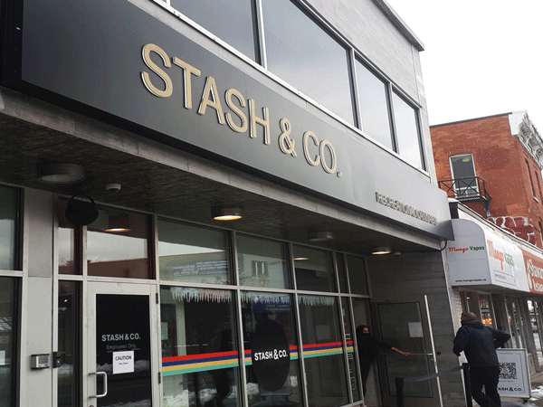 An employee of Stash & Co. holds the door open for a customer. 