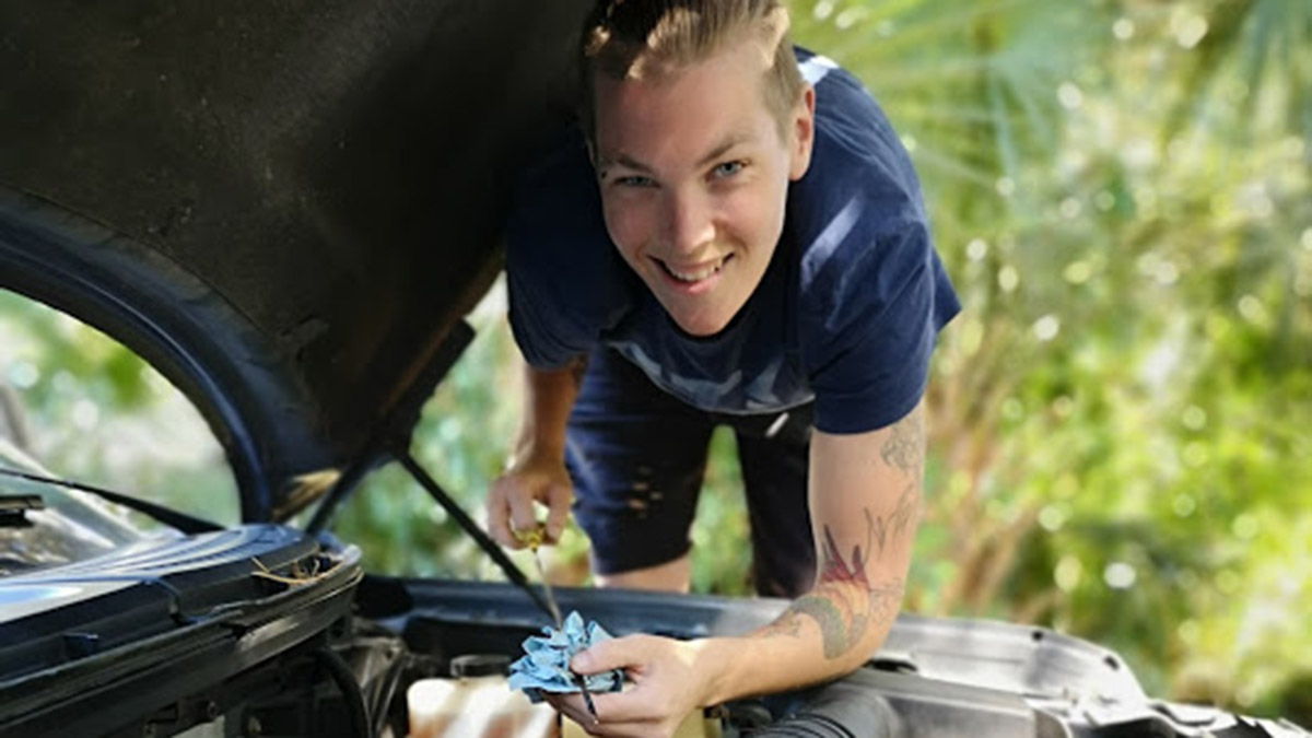 Kai Dean, smiles as they clean off an oil dipstick.