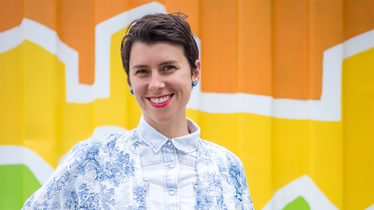 Renée Michaud smiles, standing in front of a colourful background.