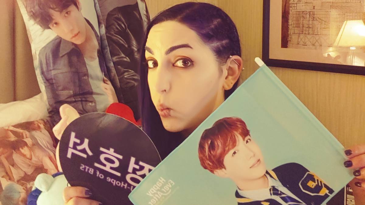 Lindsay Sherman holds up some of her BTS merch, including a flag of J-Hope and a pillow of Jungkook.