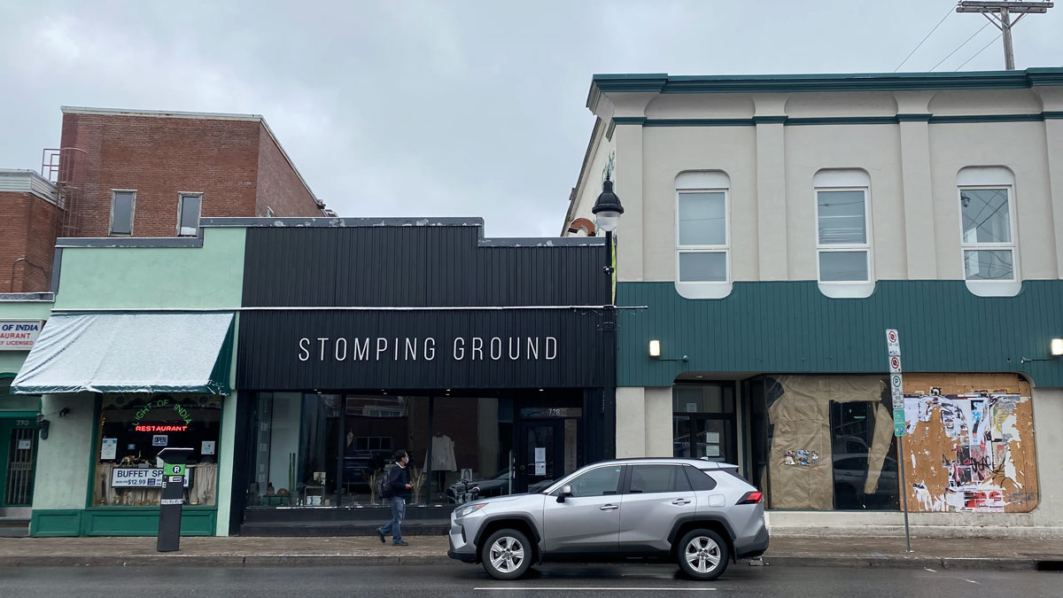 Picture of storefronts at Bank and First Street Intersection. Stores (from left to right) are: LIght of Idea, Stomping Ground, third store is bordered up and empty.