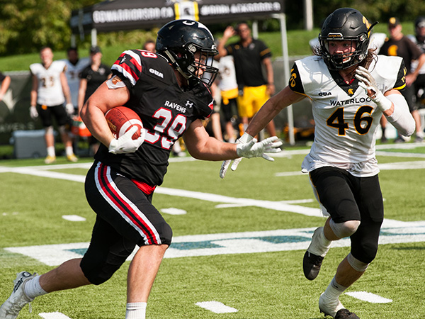 football player carries football to avoid a tackle