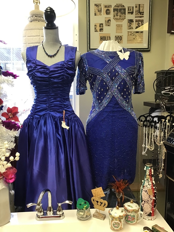 Two vintage dresses on dress mannequins surrounded by various other antiques and collectables.