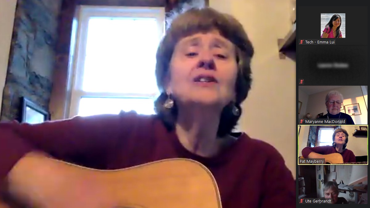 A woman strums a guitar on a zoom call.