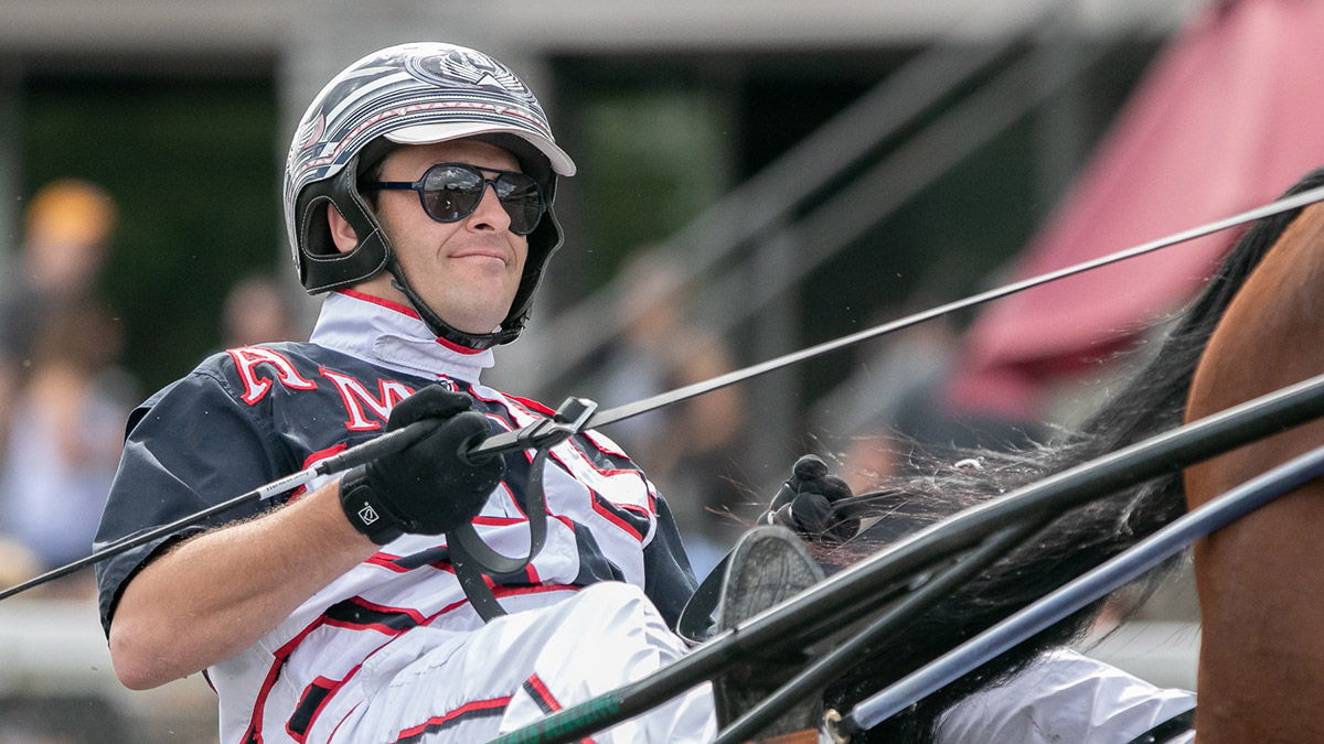 A man wearing a helmet and sunglasses sits in a cart pulled by a horse.