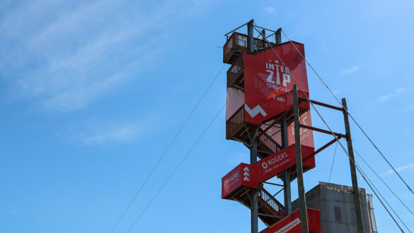 A zipline launch tower with a red banner that says "Interzip Rogers".
