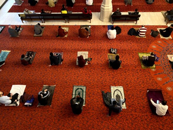 Photo taken from above, people sit on prayer mats six feet apart.