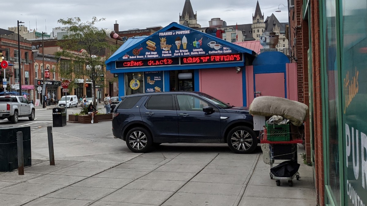 Image of a shopping cart filled belonging to an unsheltered person near a food stall in the ByWard Market on an overcast day. 