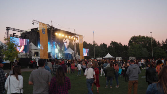 Crowd stands before the main stage at sunset.