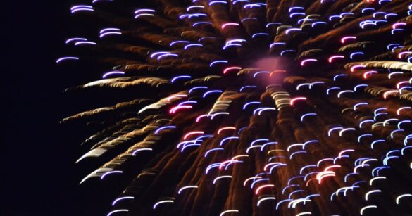 A long exposure shot of a firework exploding across the night sky in reds, blues and yellows.