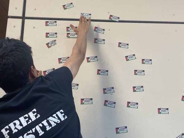 Protestor leaving stickers of the Palestinian flag that read "boycott Israeli apartheid" on a wall of the outside of the Israeli Embassy.