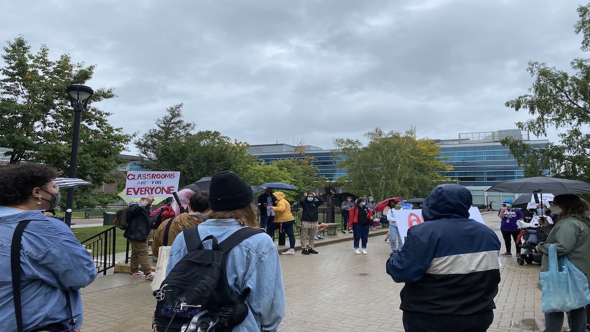 Students at the CU Care walkout in the Carleton quad on sept. 22, holding protests signs and umbrellas.