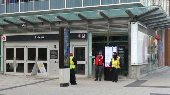 City officials wearing safety vests stand outside the closed doors of Rideau station.