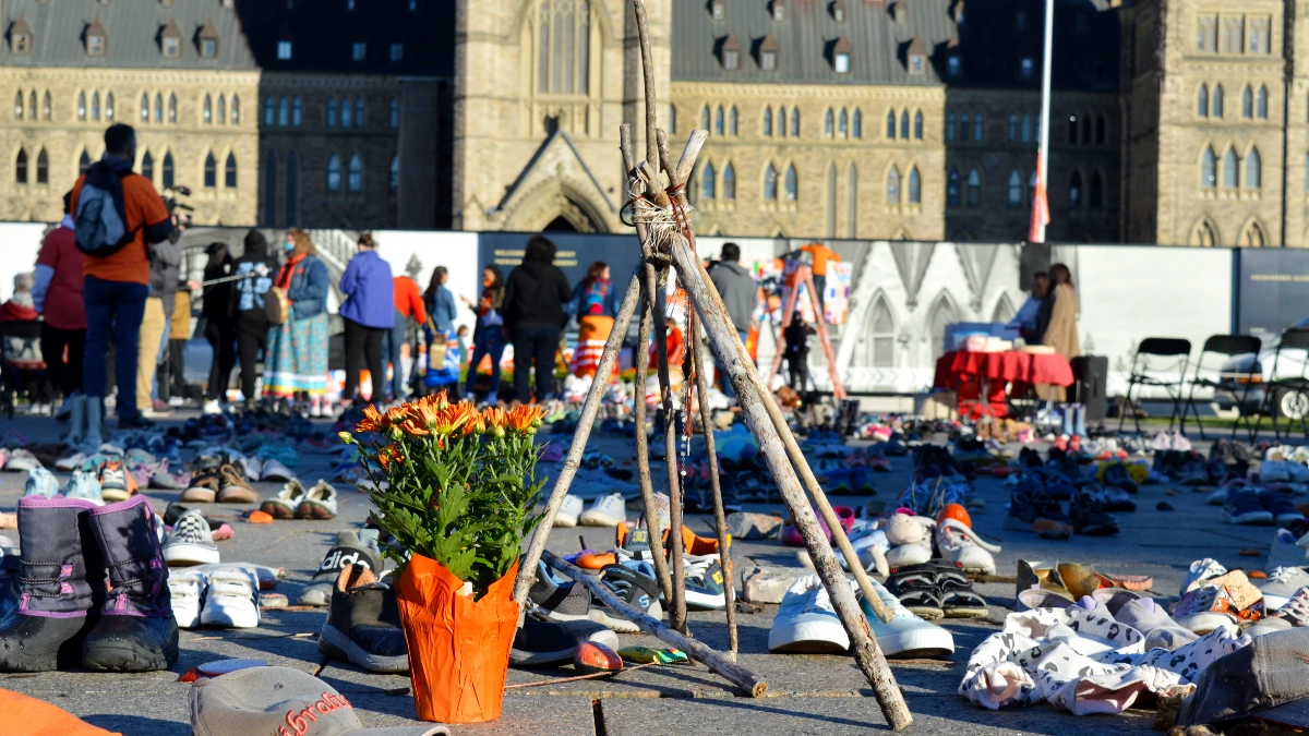 Dozens of childrens' shoes, a flower pot and a wooden structure in front of the Parliament building.