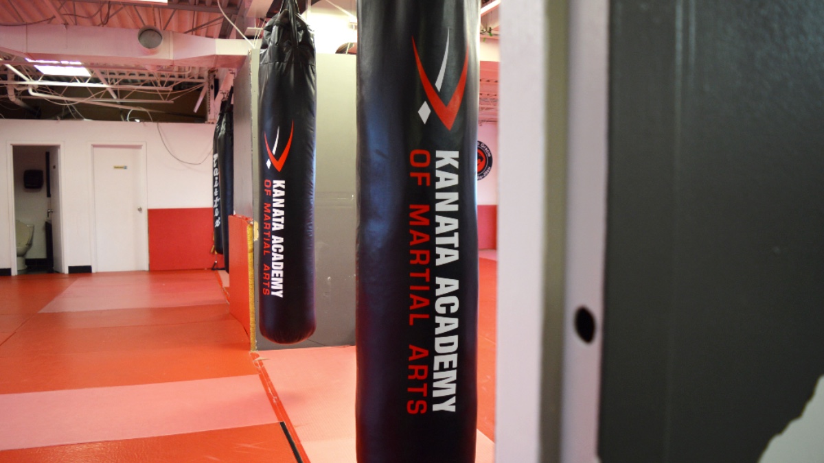 Two punching bags hang in studio with the words "Kanata Academy of Martial Arts". Floors are a bright red. 