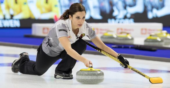 Lisa Weagle throws a yellow curling stone while holding a yellow curling broom