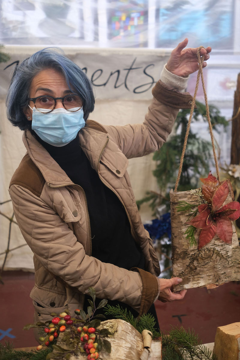 Woman with blue hair is holding up a bag made of birch at the Christmas market. The bag has a large red flower on the front.