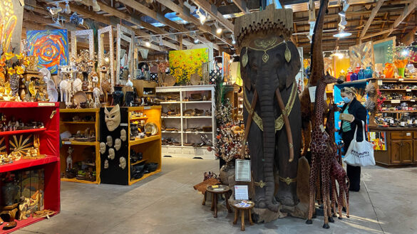 The interior of the One World Bazaar in an old barn. Tall shelves are stocked with handcrafted goods from developing nations around the world and a giant elephant, the largest item, is the centerpiece.