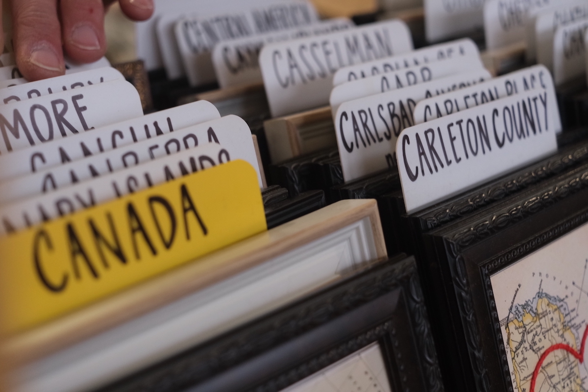 A stack of embroidered maps are stacked together. In focus are signs for maps from Canada and Carleton county.