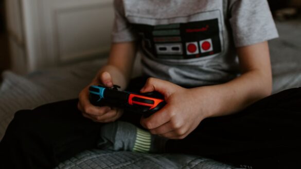 A child in a grey t-shirt playing video games, holding a gaming controller.