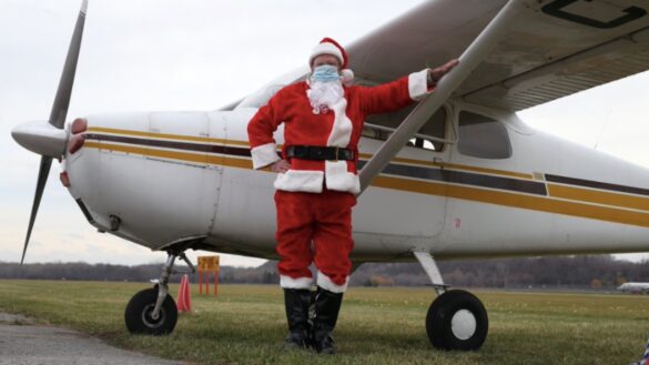 A picture of Santa Clause in front of a vintage plane.