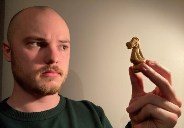 Jon curiously looks at a white knight piece from his chess set.