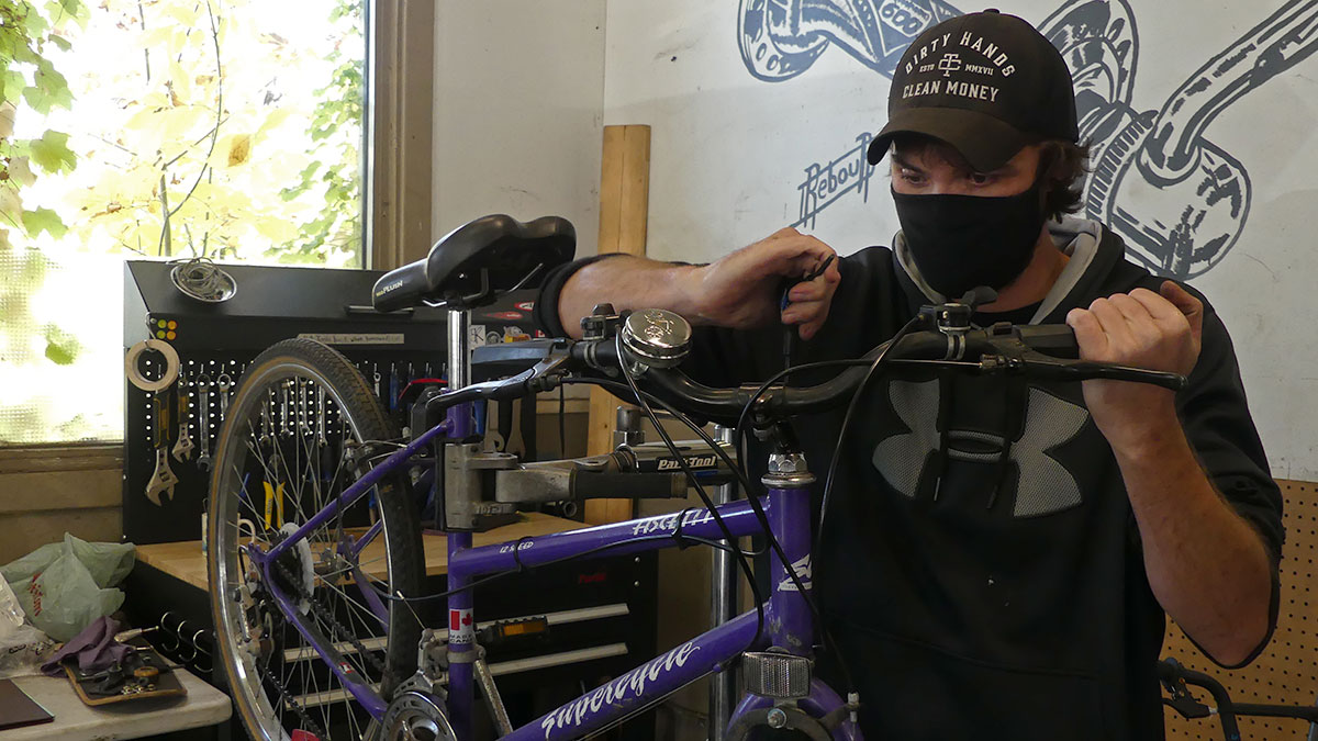 Darrin Busby, in a black cap, mask and hoodie, adjusting a purple bike's handlebars