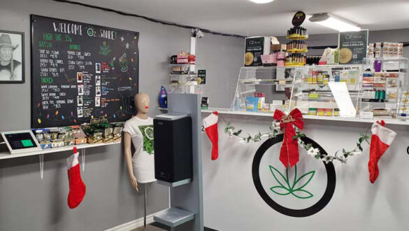 The inside of a cannabis store is shown, with a hand sanitization station in the foreground and a counter with a display full of products in the back.