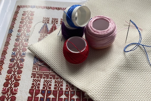 Blue, red, purple and pink thread on an empty embroidery sheet and a tatreez pattern book.