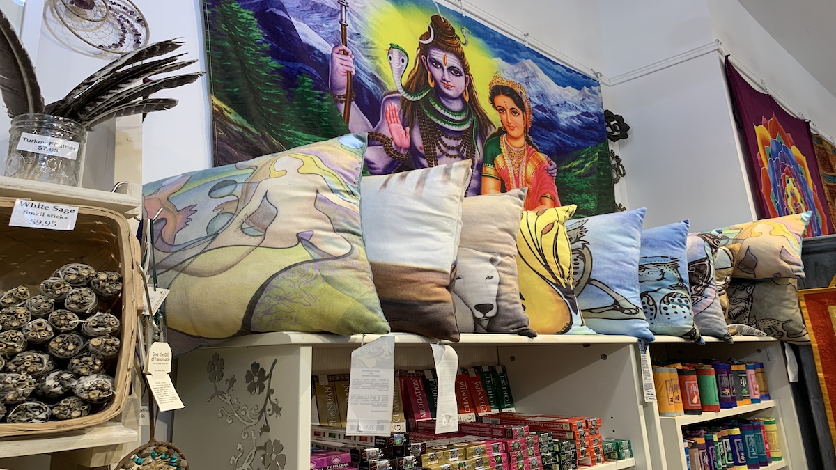 Cushions sit above a shelf surrounded by white sage, turkey feathers, tapestries and other products.