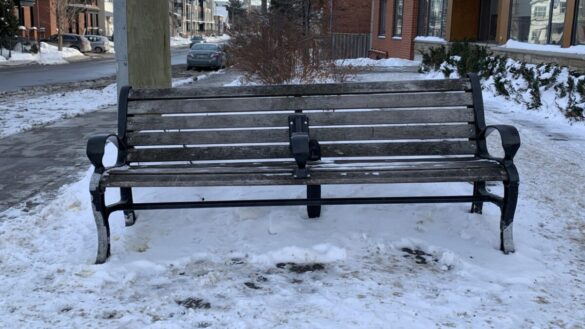 An anti-homeless bench with an arm rest placed in the middle.