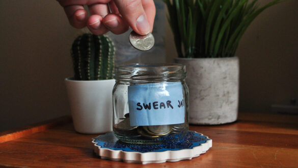 A hand drops a coin into a glass jar labelled 'swear jar'