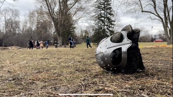 A medieval looking helmet lies on a field in front of LARPers, people who roleplay as medieval warriors.