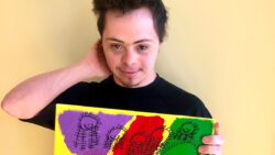 Jamensky stands against a wall holding a colourful painting