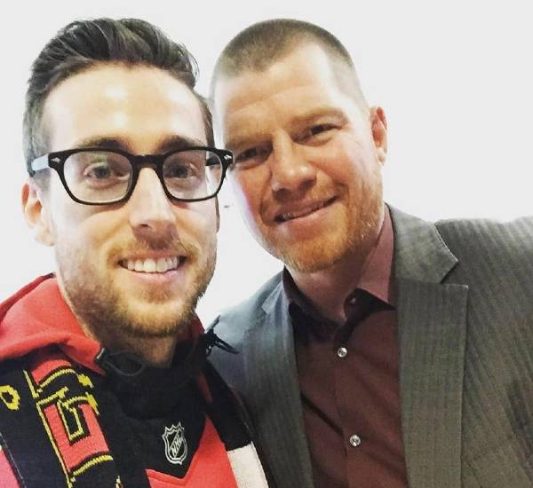 Darcy Cudmore stands in an Ottawa Senators jersey beside Chris Neil, wearing a suit.