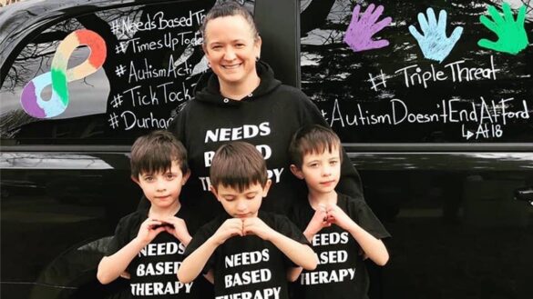 A mother stands behind her three sons wearing shirts that say "Needs based therapy".